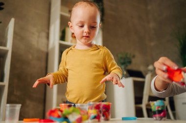 Küçük bir çocuğun portresi evde ya da kreşte renkli mankenlerle eğleniyor. Yaratıcı çocuk evde eğleniyor. Çocuk plastikle veya hamur ile oynar. Bebekler için eğitici bir oyun.