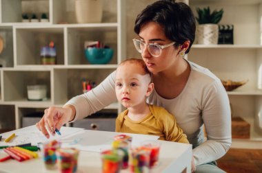 Anne ve küçük oğlu evde renkli kille oynuyor ve resim yapıyor ve birlikte resim yapıyorlar. Bebek bakıcısı kadın ya da teyzesi, eğlenirken çocuğa yardım ediyor. Mutlu bir aile. Boşluğu kopyala.