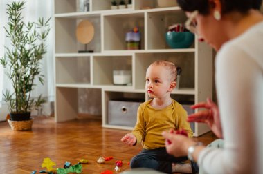 Tatlı çocuk ve bekar annesi yerde oturup yaratıcı aktivitelerle meşgul olarak eğleniyorlar. Kil dökerken bir çocuğa yardım eden bebek bakıcısı ya da teyze. Anaokulunda oynuyorum. Bir çocuğa odaklan..