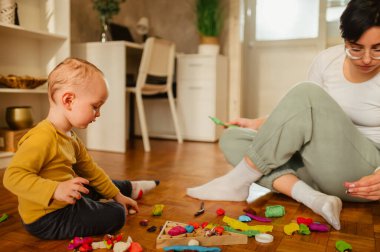 Gülümseyen bebek bakıcısı ya da bir çocukla yerde oturup kille oynayan dadı. Anne çocuk renklerini öğretmeye yardım eder. Çocuk gelişimi. Bir çocuğa odaklan. Boşluğu kopyala.