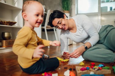 Oğlu ve annesi yerde otururken kil kalıpları döküyorlar. Evde yaratıcı aile aktiviteleri. Bebek bakıcısı ya da teyze küçük çocukla oynarken ve öğrenirken eğleniyor. Bir kadına odaklan..
