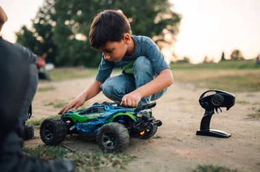 Genç çocuk uzaktan kumandalı elektrikli yarış arabasının önünde çömelmiş babasıyla oynayacağı oyun seansına hazırlanıyor. Bir çocuk babasıyla maça hazırlanıyor..