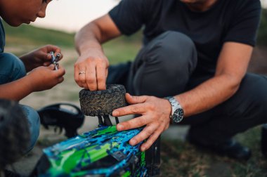 Oğlu onlara yardım ederken babası tarafından tamir edilen kırık bir oyuncak araba üzerine seçici bir odaklanma. Babanın ve oğlunun ellerine odaklan. Baba cıvatayı düzüyor ve oğlu da vida aletini tutuyor..