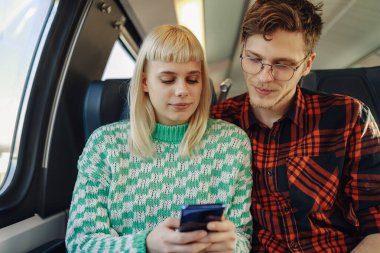 Trende oturan hippi banliyö sakinleri seyahat sırasında telefonda yazarlar ve telefona bakarlar. Genç bir şehir çifti trenle seyahat ediyor ve internet üzerinden mesajlaşmak için cep telefonu kullanıyor.