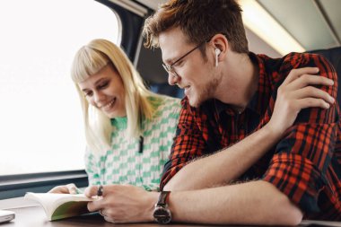 Genç ve mutlu bir hippi çift trende oturuyor ve yolculukları sırasında kitap okuyor. Trenle seyahat eden ve seyahat ederken kitap okuyan neşeli gezginlerin portresi. Trendeki çift..