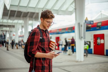 Metro istasyonunda elinde hazır kahveyle duran ve telefonuna online mesajlar yazan genç bir yolcunun portresi. Şehir dışından bir yolcu metro istasyonunda tren bekliyor. Boşluğu kopyala