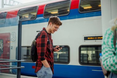 Bir şehir yolcusu metro istasyonunda duruyor ve telefonuna gülümserken metro istasyonunu bekliyor. Trenin yanında son moda bir yolcu duruyor ve ona gülümserken telefonuna mesaj yazıyor..