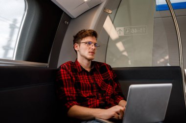 Genç bir trend yolcusu işe giderken metroya biniyor ve dizüstü bilgisayarla çalışıyor. Genç bir işçi metro treninde dizüstü bilgisayarda yazı yazıyor. Trende dizüstü bilgisayarda çalışan bir şehir yolcusu..