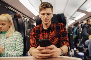 Trenle seyahat eden ve cep telefonu kullanan genç bir hippinin portresi. Bir gezgin demiryolu aracında oturuyor ve telefonda yazıyor. Bir adam trenle uzak bir yerde seyahat ediyor.