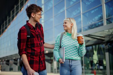 Üniversite kampüsünde durup birbirlerine gülümseyen öğrenciler. Üniversite binasının önünde durup konuşan mutlu bir üniversite öğrencisi. Bir kız dizüstü bilgisayar taşırken bir erkek....