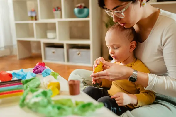 Bebek bakıcısı ya da dadı yerde oturup kille oynarken küçük çocukla oynuyor. Anne çocuğa renkleri ve farklı şekilleri nasıl şekillendireceğini öğretir. Çocuk gelişimi. Boşluğu kopyala.