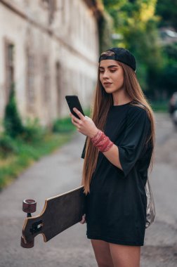 Longobard 'ını tutan ve yolda yürürken akıllı telefon kullanan genç bir kadın.