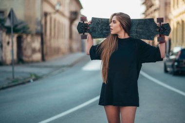 Genç bir kadın uzun panosunu tutuyor ve şehirde yolun ortasında duruyor.