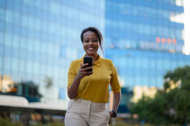 Güzel, genç, Afro-Amerikalı bir kadın şehirde akıllı telefon kullanıyor.