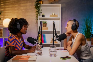 İki ırklar arası içerik yaratıcısı, mikrofon açık ve mikrofon başında bir kayıt stüdyosunda oturmuş konuları tartışıyorlar. İki kız internet için canlı yayın yapıyor..