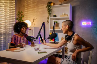 İki ırklar arası podcaster, evde bir podcast stüdyosunda, kulaklıkları açık ve telefonda içeriği tartışıyorlar. Vlog yazarları sosyal medya için bir bölüm çekiyor.
