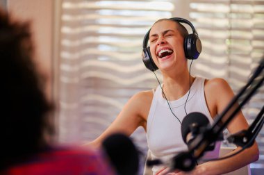 Ev kayıt stüdyosunda kulaklıkla oturup gülerek ve eğlenerek podcast yapan bir röportajcının portresi. Neşeli bir podcaster podcast programı sırasında gülüyor..