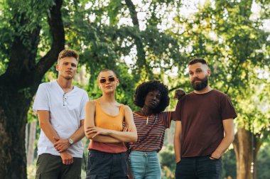 Şehir parkında durup kameraya bakarken poz veren çok kültürlü gençlerin portresi. Doğadaki genç ırklar arası arkadaşlar kameraya bakıyor. Çeşitlilik ve birlik kavramı. Boşluğu kopyala.