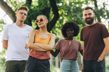 Genç ırklar arası alternatif arkadaşlar kameraya bakıp gülümsüyor. Şehir parkında kameraya poz veren genç alt kültür ekibinin portresi. Moda ve şehirli arkadaşlar kameraya gülümsüyor..