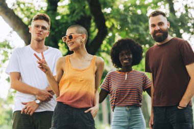 Şehir parkında durup kameraya gülümserken poz veren çok kültürlü doğa severlerin portresi. Doğada kameraya gülümseyen çok az ırklar arası arkadaş var. Şehir parkında çeşitli alternatif arkadaşlar.