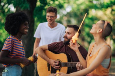 Parkta oturup gitar çalan ve eğlenen çok kültürlü sokak sanatçılarının portresi. Müzisyenler halk parkında doğaçlama yapıyorlar. Parkta prova yapan göstericilerin portresi.