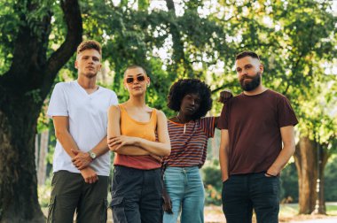 Şehir parkında birlikte duran ve poz veren çok kültürlü küçük bir arkadaş grubunun portresi. Parkta durup kameraya bakan havalı hippi bir arkadaş. Şehir parkında poz veren arkadaşlar.