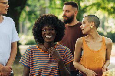 Afro-Amerikan bir kızın portresi. Bir şehir parkında ekibiyle dikiliyor ve başka tarafa bakarken gülümsüyor. Irklar arası trend hipster arkadaş grubu şehir parkında birlikte kaliteli zaman geçiriyorlar..
