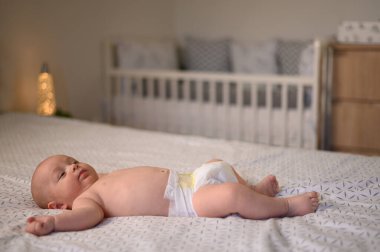 Yatak odasında bebek bezi takmış, sırtüstü uzanmış.