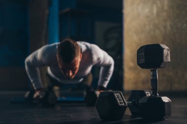 Spor salonunda antrenman yaparken halterle şınav çeken kaslı yakışıklı bir adam.