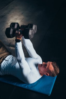 Spor salonunda antrenman yaparken kaslı yakışıklı adam dambılı kaldırıyor.