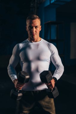 Spor salonunda antrenman yaparken kaslı yakışıklı adam dambılları kaldırıyor.