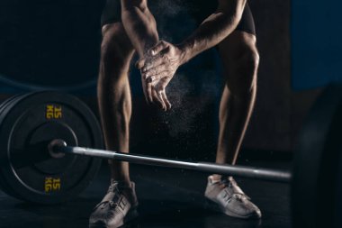 Üzerinde tebeşir olan el çırparken halterini kaldıran sağlıklı genç bir adamın kırpılmış görüntüsü.