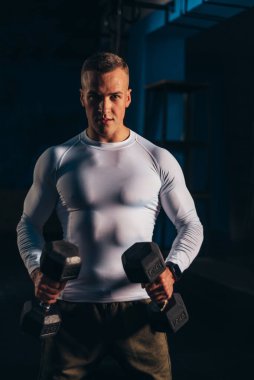 Spor salonunda antreman yaparken dambıl tutan çekici bir genç.