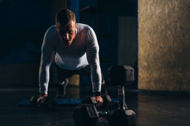 Salonda dambıl tutarken ve antrenman yaparken şınav çeken çekici bir adam.