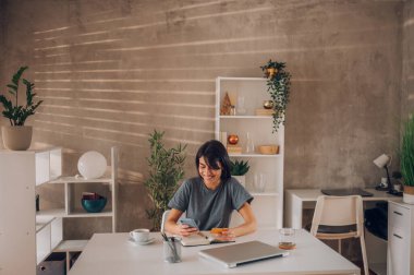 Kafkasyalı genç bir iş kadınının yüzünde büyük bir gülümsemeyle cep telefonuna baktığı ve sipariş parasını öderken kredi kartı numarasını yazdığı geniş açılı bir görüntü. Boşluğu kopyala.