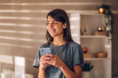 Güneşli evinde elinde cep telefonuyla duran güzel beyaz bir iş kadınının portresi. Kenara bak ve gülümse. Başarılı bir iş gününün tadını çıkarıyorum..