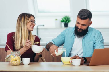 Gülümseyen genç bir çiftin mutfakta kahvaltının keyfini çıkarırken.