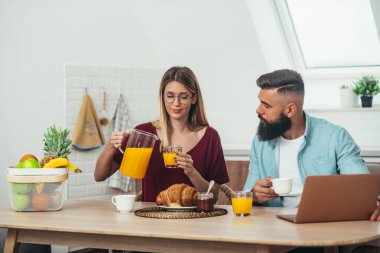 Evdeki mutfakta kahvaltı sırasında birlikte kahve içen genç bir çiftin fotoğrafı.
