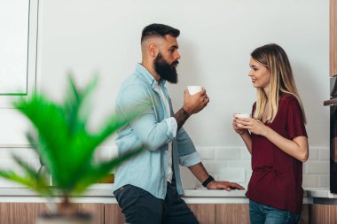 Sabahları mutfakta kahve içen genç bir çiftin fotoğrafı.