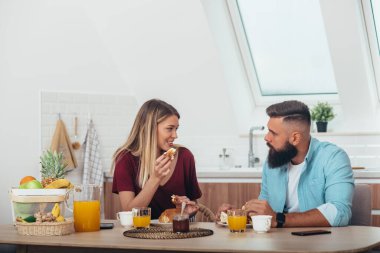 Evde ayçöreği yerken mutfakta kahvaltı eden bir çift.