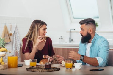 Evde kruvasan yiyip kahve içen genç bir çiftin fotoğrafı.