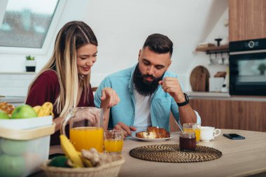 Genç bir çiftin evdeki mutfakta kahvaltının tadını çıkarırken çekilmiş bir fotoğrafı.