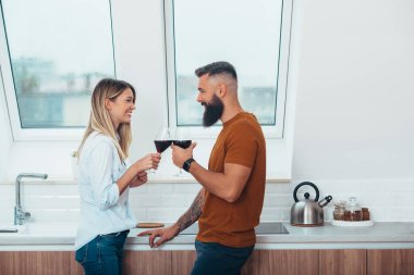 Evlerinin mutfağında şarap içen genç bir çiftin fotoğrafı.