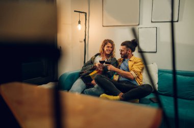 Genç bir çiftin rahat bir kulübede oturup şarap içerken geniş bir görüntüsü. Tatil günlerinin tadını çıkarırken birlikte iyi vakit geçiriyorlar. Genç sarışın kız büyük gülümsemeli çocuğa bakıyor. Boşluğu kopyala.