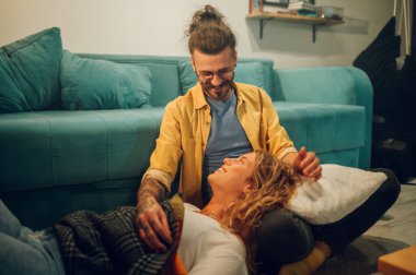 Sevgilisi kucağında başıyla yerde yatarken genç ve mutlu bir adamın zeka kadehinin geniş açılı görüntüsü. Hem gülüyor, hem de eğlenirken birbirlerine bakıyorlardı. Boşluğu kopyala.