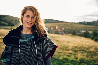 Sıcak güneşli bir günde güzel dağ yolunda yürüyüş yapan ve kameraya bakarken poz veren gülümseyen kadın gezgin. Kırsalda tatilde olan mutlu genç bir bayan. Seyahat ve macera konsepti.