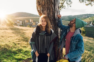Genç çift dağ yolunda yürürken ve ağacın altında dinlenirken yürüyüş yaparken eğleniyor. Kameraya bakan beyaz, sarışın bir kadına odaklan. Boşluğu kopyala.