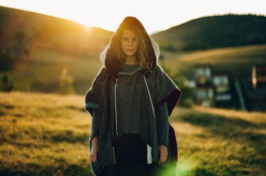 Sıcak güneşli bir günde, güzel dağ yolunda yürüyüş yapan ve kameraya bakarken poz veren kalın örülü elbiseli bir kadının portresi. Kırsalda tatilde olan mutlu genç bir bayan. Güneş parlaması.