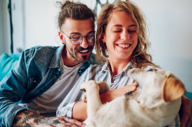 Çift sarı labrador köpeklerini evdeki kanepede okşuyor. Kanepede oturan mutlu bir adam ve yanında oturan güzel bir kız arkadaşı olan evcil bir köpeğe sarılıyor. Birkaç tanesine odaklan. Boşluğu kopyala.