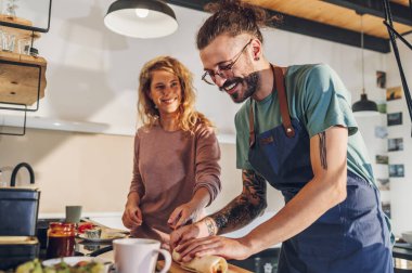 Önlük takan yakışıklı genç bir adam ve güzel bir kız mutfakta yemek pişiriyor. Mutlu çift sağlıklı organik yemek hazırlıyor. Kahvaltı ya da akşam yemeği için burrito yapıyorum..